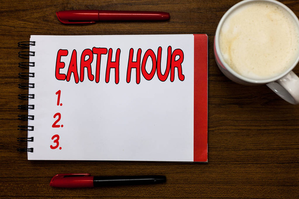 Käsiala kirjoittaminen Earth Hour. Käsitteen merkitys Globaali liike vaatia suurempia toimia ilmastonmuutoksen torjumiseksi Avaa muistikirja merkit inspiraatio kommunikoida ideoita puinen pöytä cup kahvia
. - Valokuva, kuva