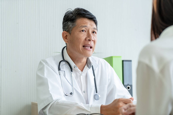 Asijské starší lékař a pacient jednají něco, zatímco sedí u stolu - Fotografie, Obrázek