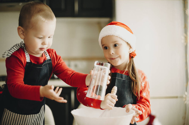 Menina adorável em chapéu de Papai Noel e menino infantil trabalhando em equipe e fazendo biscoitos de férias
 - Foto, Imagem