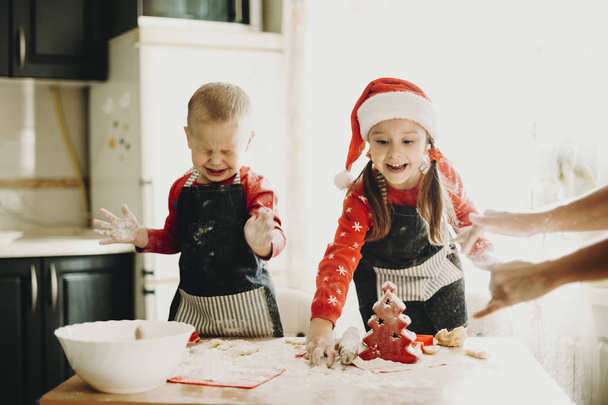 Charming little boy and girl at table in kitchen preparing for Christmas holiday making cookies with mother - Fotó, kép