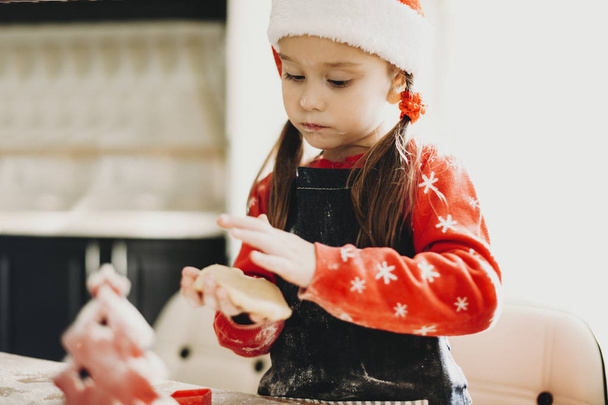 Niña usando sombrero de Santa con delantal y haciendo galletas para las vacaciones de Navidad
 - Foto, Imagen