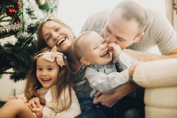 Happy familiy embracing each other and lauching near Christmas tree - Photo, Image