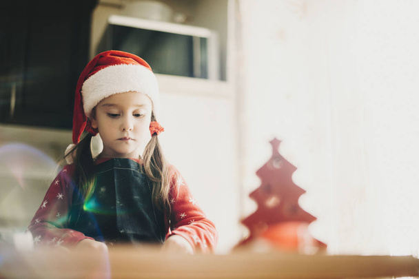 De baixo de menina bonita vestindo chapéu de Papai Noel enquanto estava à mesa na cozinha fazendo biscoitos
 - Foto, Imagem