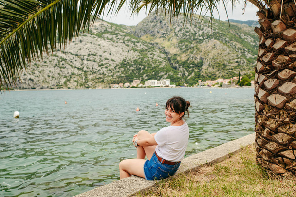 Женщина, сидящая на берегу, смотрит на волны. горы на заднем плане. летнее время
 - Фото, изображение
