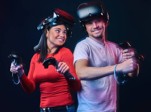 Jovem casal sorrindo se divertindo juntos, brincar com fones de ouvido VR e controladores
. - Foto, Imagem