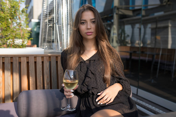 Young woman sitting on the terrace of a restaurant with a glass of wine. - Fotó, kép