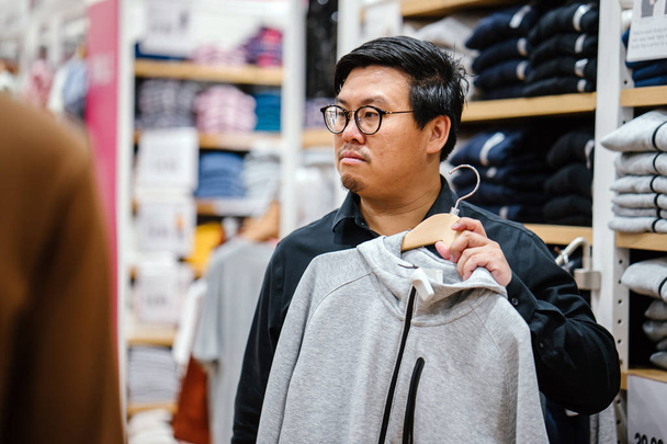 A middle-aged Chinese man is shopping for clothing in a fast fashion store.  - Foto, imagen