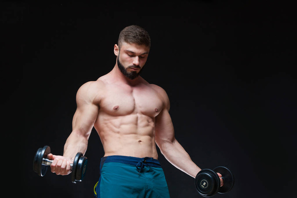 Muscular bodybuilder guy doing exercises with dumbbell over black background - Foto, imagen