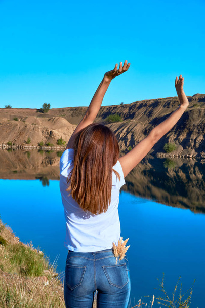 young beautiful girl doing exercises and stretching on a rock overlooking a clear blue lake on a clear sunny day - 写真・画像
