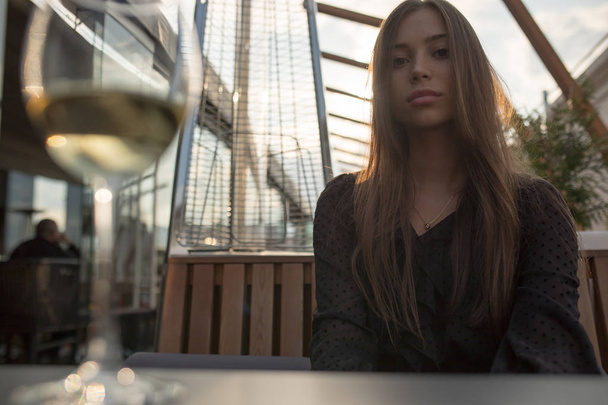 Young woman sitting at a table on the terrace of a restaurant with a glass of wine. - Fotoğraf, Görsel