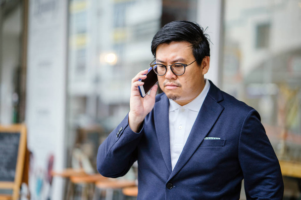 Portrait of a middle-aged Chinese Asian man in a casual suit. He is talking on his phone  - Fotografie, Obrázek