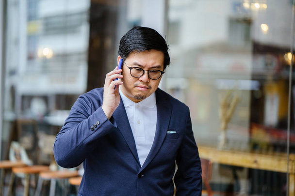Portrait of a middle-aged Chinese Asian man in a casual suit. He is talking on his phone  - 写真・画像