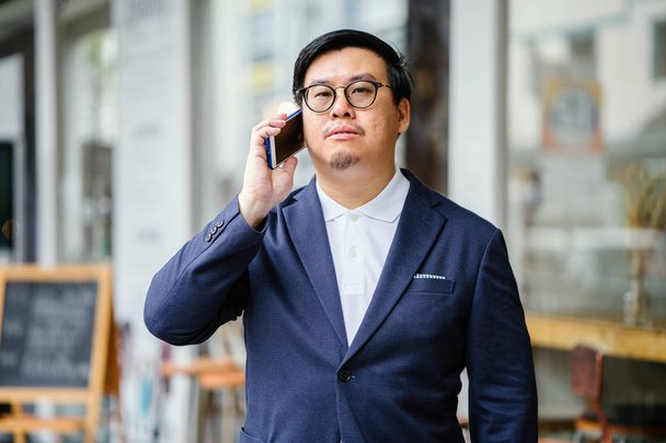 Portrait of a middle-aged Chinese Asian man in a casual suit. He is talking on his phone  - Foto, imagen