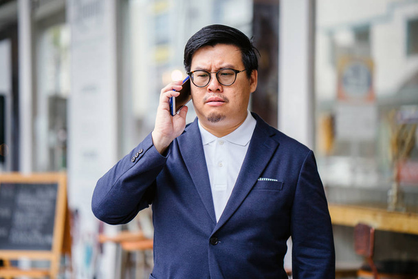 Portrait of a middle-aged Chinese Asian man in a casual suit. He is talking on his phone  - Foto, Imagen