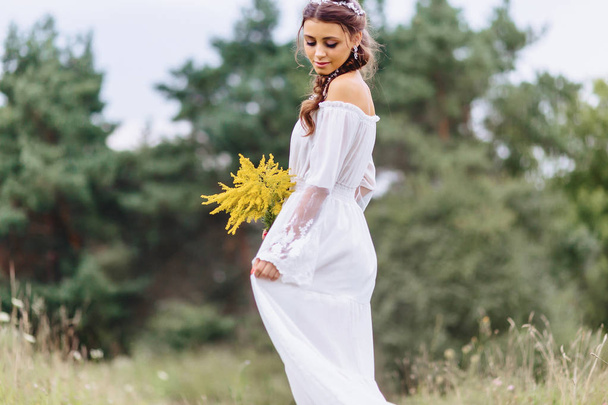 joven bonita chica con flor en sus manos en vestidor ligero caminar en el césped cerca de verde bosque de verano
 - Foto, imagen