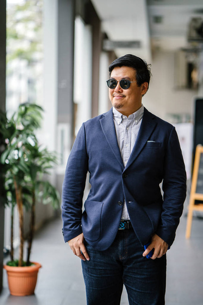 Portrait of a middle-aged Chinese Asian man (Singaporean) in smart casual standing in the city. He is well-dressed and groomed in a navy suit, oxford button-down shirt  with sunglasses. - Photo, Image