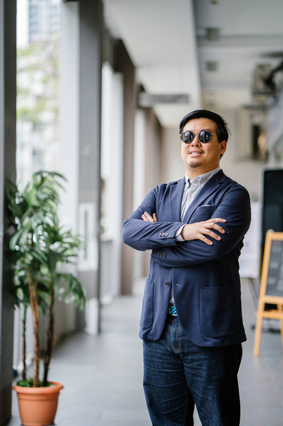 Portrait of a middle-aged Chinese Asian man (Singaporean) in smart casual standing in the city. He is well-dressed and groomed in a navy suit, oxford button-down shirt  with sunglasses. - Photo, image