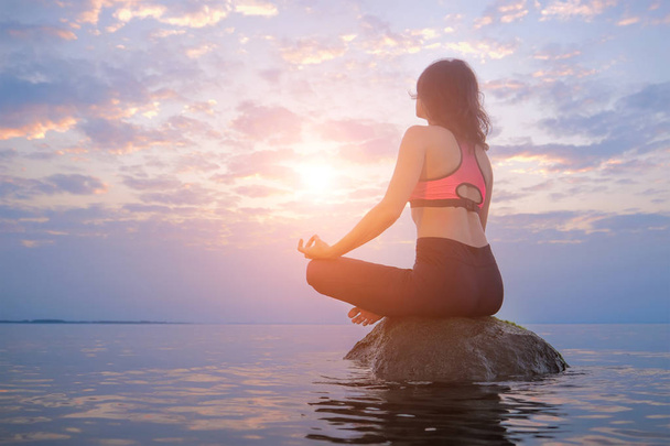 Nainen istuu kivellä meressä. Meditointi ja rentouttava käsite
. - Valokuva, kuva