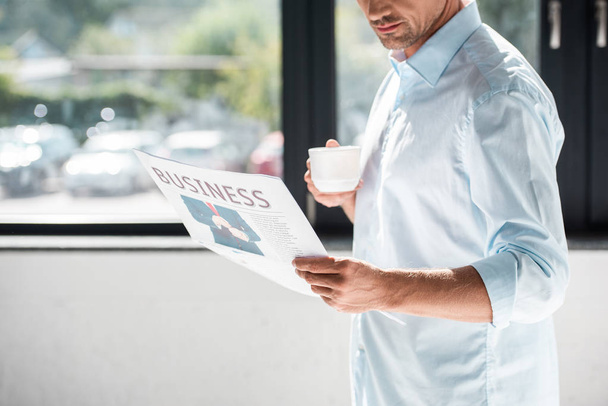 cropped shot of handsome adult businessman in shirt drinking coffee and reading newspaper - Foto, Imagen