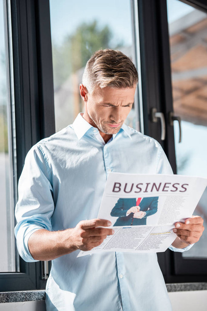 ernsthafter erwachsener Geschäftsmann liest Wirtschaftszeitung vor dem Fenster - Foto, Bild