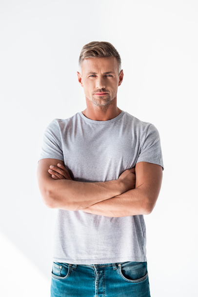 handsome adult man in blank grey t-shirt looking at camera with crossed arms isolated on white - Foto, imagen