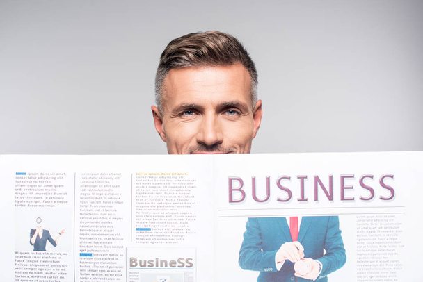 close-up shot of handsome adult businessman covering face with business newspaper isolated on white - Foto, afbeelding