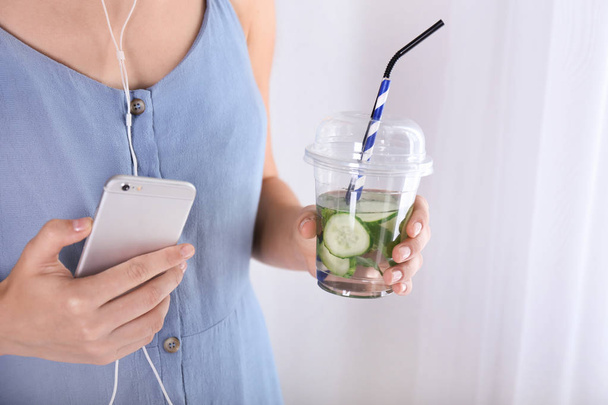 Lezzetli taze salatalık suyu ve cep telefonu, closeup ile plastik bardak tutan kadın - Fotoğraf, Görsel