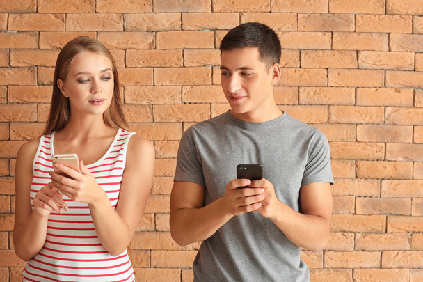 Young couple with mobile phones against brick wall - Foto, afbeelding