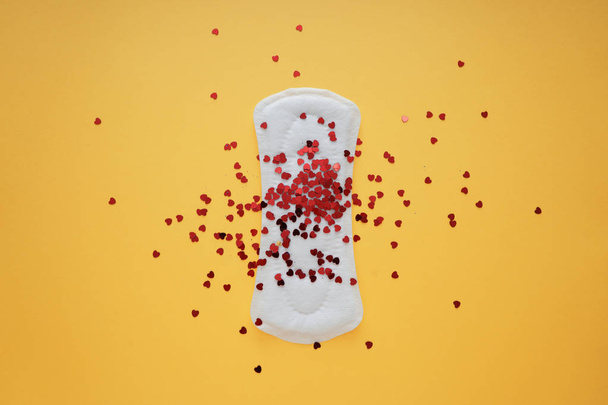 Менструальная прокладка с маленькими красными сердцами на цветном фоне
 - Фото, изображение