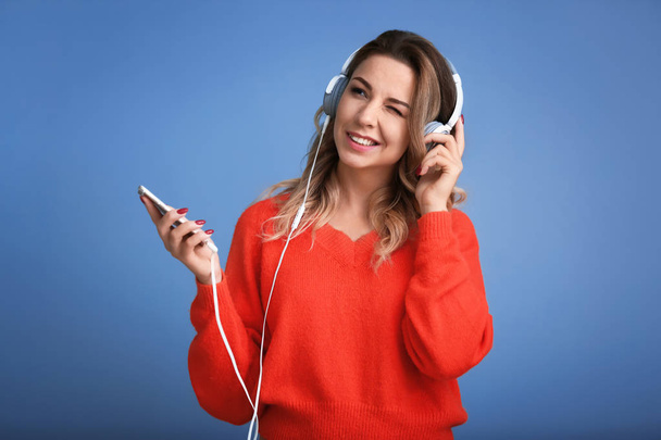Portret van mooie jonge vrouw luisteren naar muziek op kleur achtergrond - Foto, afbeelding