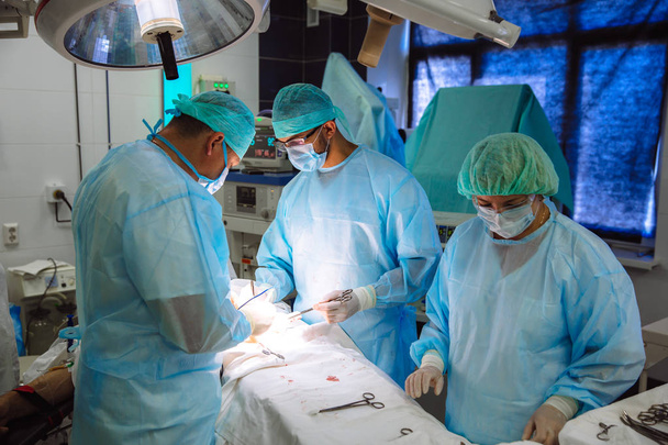 Une équipe de médecins en vêtements médicaux stériles effectue une opération dans un hôpital. Travail professionnel à la clinique, les chirurgiens sont des hommes avec une assistante. Le concept de santé, médecine
. - Photo, image