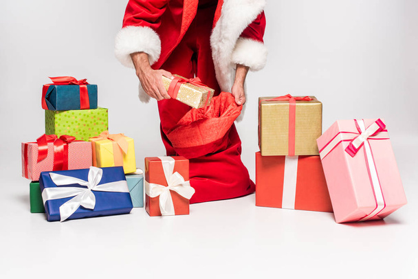 cropped shot of santa claus packing gifts in red bag on grey - Foto, Bild