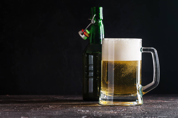 軽めのビールと暗い背景の上にボトルのガラス マグカップ - 写真・画像