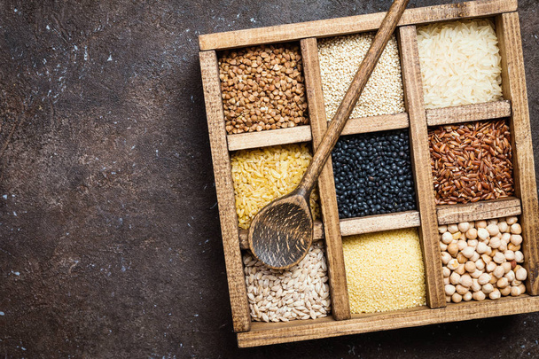 surtido de diferentes cereales y semillas en una caja sobre fondo marrón oscuro, vista superior
 - Foto, Imagen