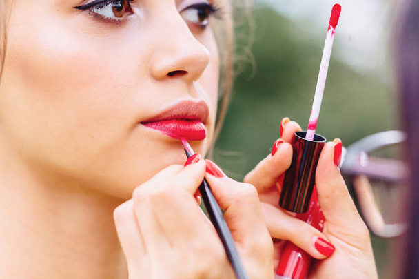 girl paints lips in red on summer street - Fotografie, Obrázek