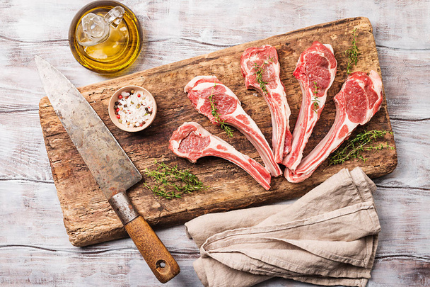 Raw lamb chops with salt, pepper and herbs over white wooden background with vintage chef knife near. Top view. - Foto, Bild