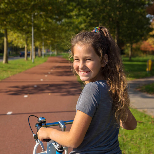 Ευτυχισμένο παιδί βόλτες με ένα ποδήλατο σε ένα μονοπάτι ποδήλατο. Ποδηλάτης παιδί ή έφηβο κορίτσι απολαμβάνει καλές καιρικές συνθήκες και την ποδηλασία. Φιλικό προς το περιβάλλον μεταφορών έννοια. Κοπέλα χαμογελάει, είναι χαρούμενη. - Φωτογραφία, εικόνα