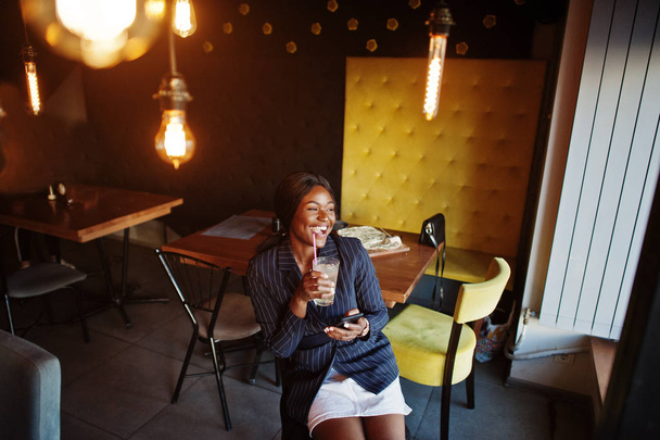 African american businesswoman drinking cocktail lemonade in cafe. Black girl having rest with mobile phone. - 写真・画像
