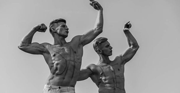 Men muscular with nude sexy torso, sky on background. Athletes with inscription sale on muscular chests. Athletes on serious faces demonstrating strength and power of their muscles. Sales concept - Photo, image