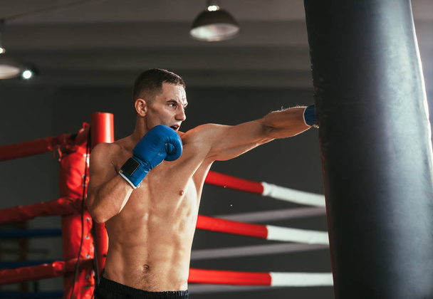 Male boxer hitting punching bag at boxing studio. Sport training concept - Zdjęcie, obraz