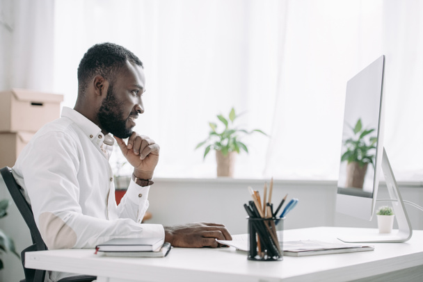 vista lateral do empresário afro-americano bonito alegre que trabalha no computador no escritório
 - Foto, Imagem