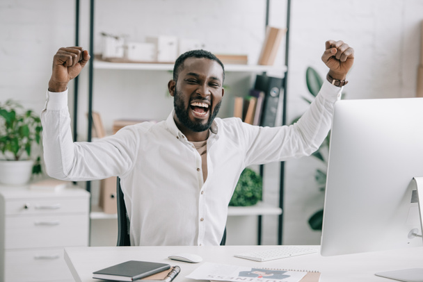 Empresário afro-americano animado gritando e mostrando sim gesto no cargo. Homem comemora ganhar uma aposta com um jogo, aposta de futebol, jogo esportivo
 - Foto, Imagem