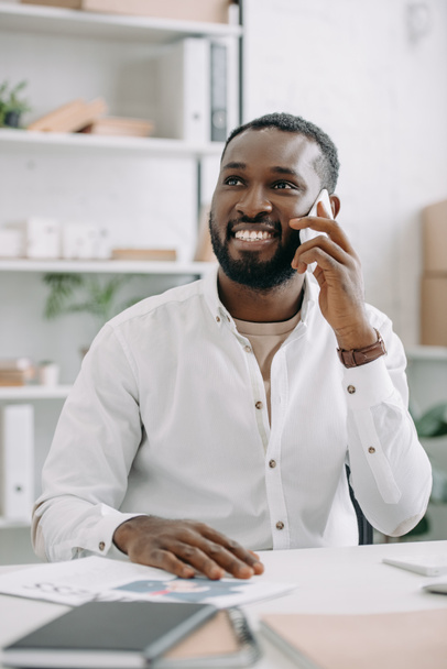 sorrindo bonito empresário afro-americano falando por smartphone no escritório e olhando para cima
 - Foto, Imagem