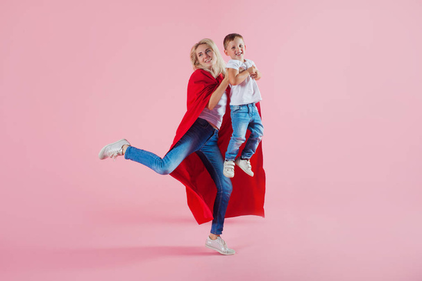 super mom. Fun family, a young blond woman in a red Cape and her son jumps and takes off - Foto, Bild