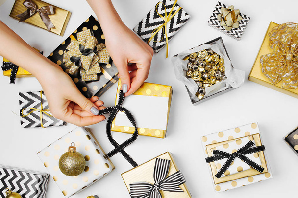 female hands attaching bow to gift box surrounded by presents - Foto, Imagen