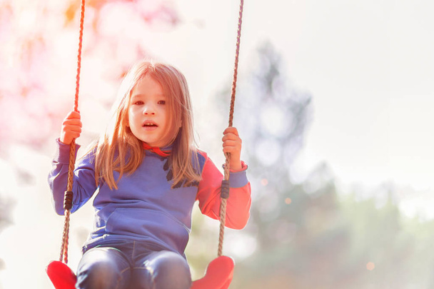 Swinging girl. Little kid having fun on a playground outdoors in summer - Foto, Bild