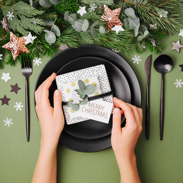 Female hands holding gift on plates with Christmas decorations on table - Photo, Image