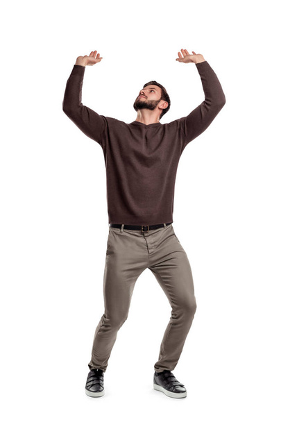 A bearded man in casual clothes attempts to hold something heavy from above on a white background. - Foto, Imagen