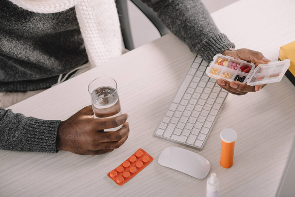 vista recortada de empresario enfermo con pastillas y vaso de agua sentado en el lugar de trabajo
 - Foto, Imagen