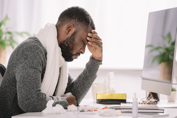 hombre afroamericano cansado con dolor de cabeza sentado en la oficina con el tratamiento y la computadora
 - Foto, Imagen